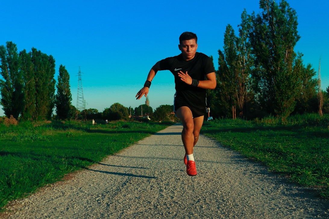Manlig löpare i svarta Nike-träningskläder som sprintar på en asfalterad stig i ett grönområde under gyllene timmen.